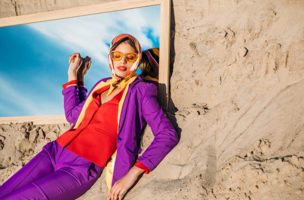 Woman leaning against house wearing sunglasses and designer clothing